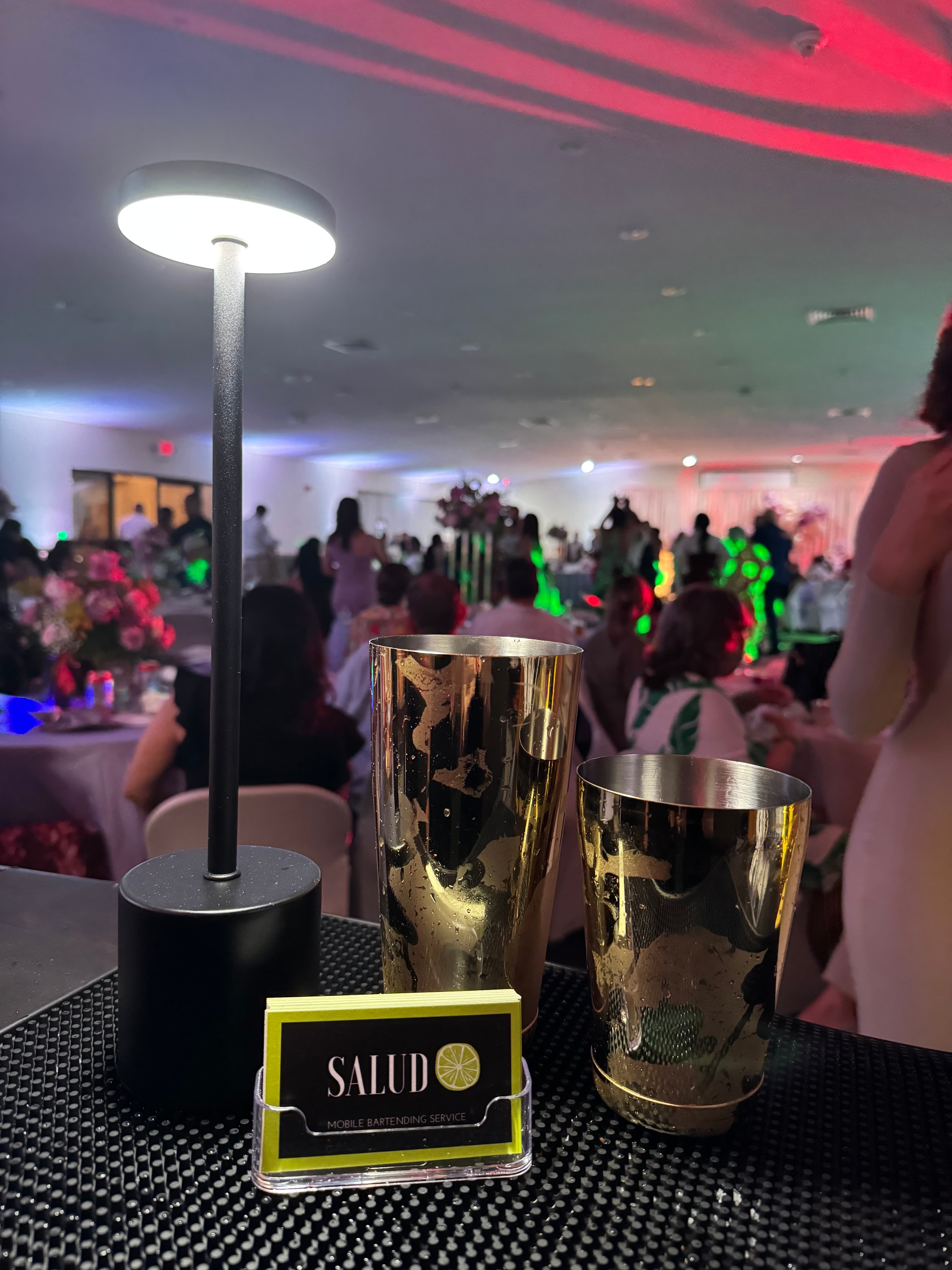 Gold cocktail shakers displayed on a bar at an event with guests in the background
