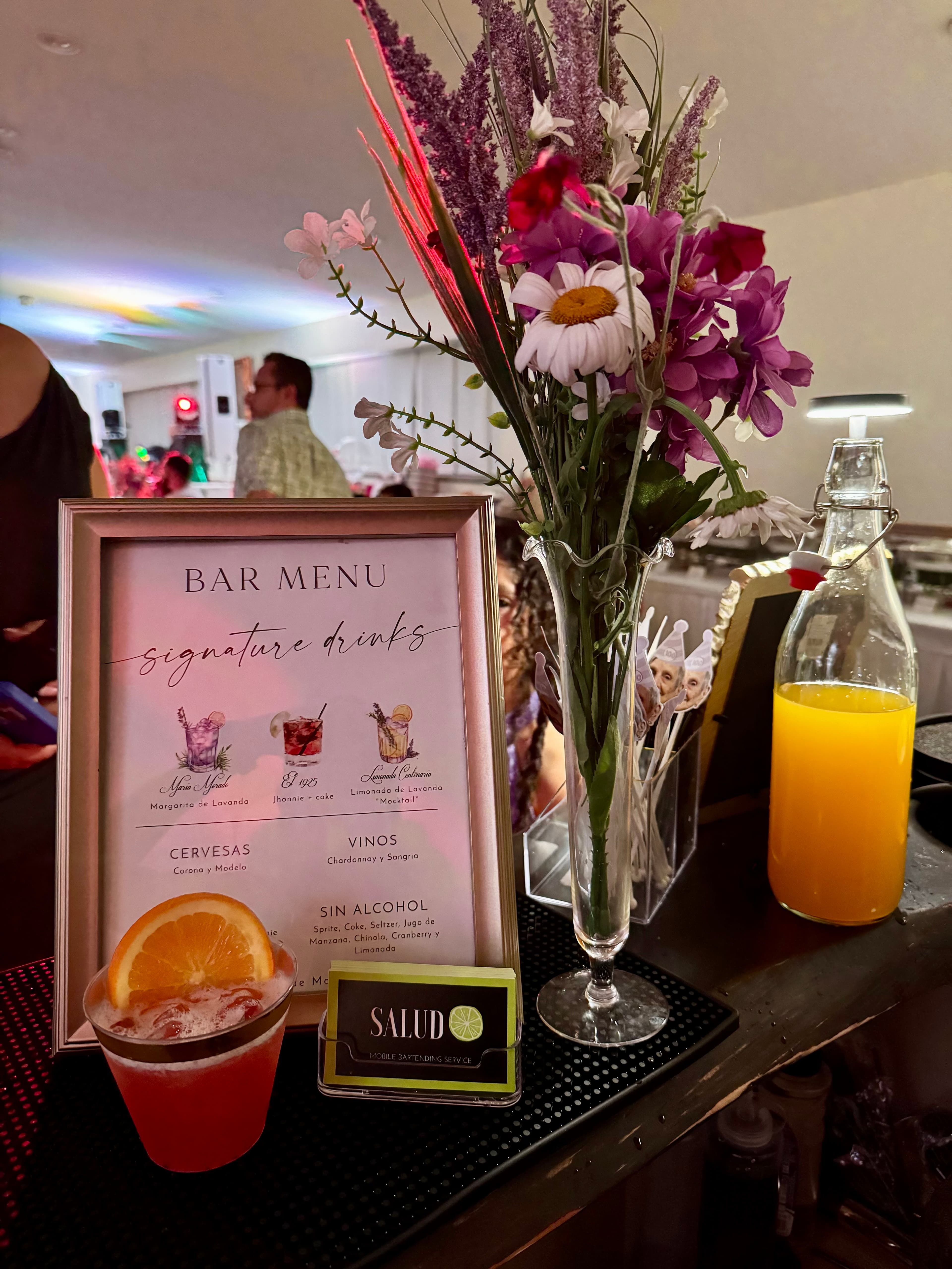 A cocktail displayed beside a bar menu with flowers on a decorated drink station.